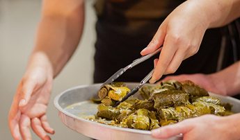 An image of A Shared Table event, showing a person serving dolmates on a plate with tongs.