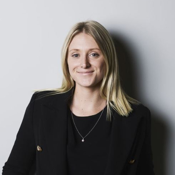 An image headshot of Sarah Chapman. Sarah has blonde shoulder-length hair and is wearing a black shirt and jacket. Sarah is smiling at the camera.